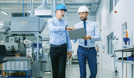 Back View of the Head of the Project Holds Laptop and Discussing Product Details with Chief Engineer while They Walk Through Modern Factory.