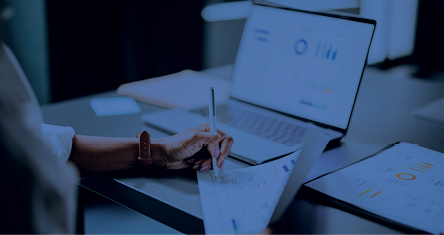 High angle view of an anonymous African-American woman analyzing business graph on a laptop computer while sitting at restaurant desk and writing notes.
