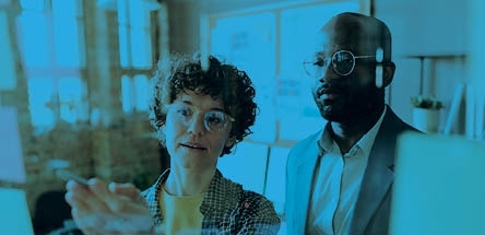 Young businesswoman discussing plans on sticky notes hanging on glass wall together with her colleague at office